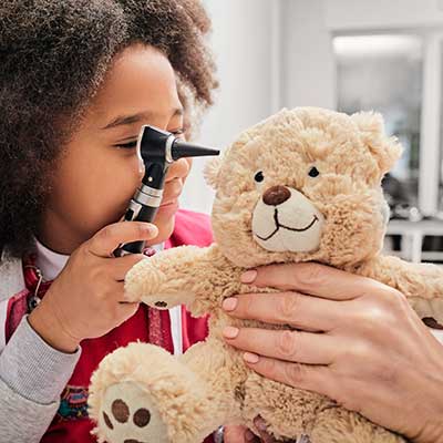 Child playing with an otoscope and bear.